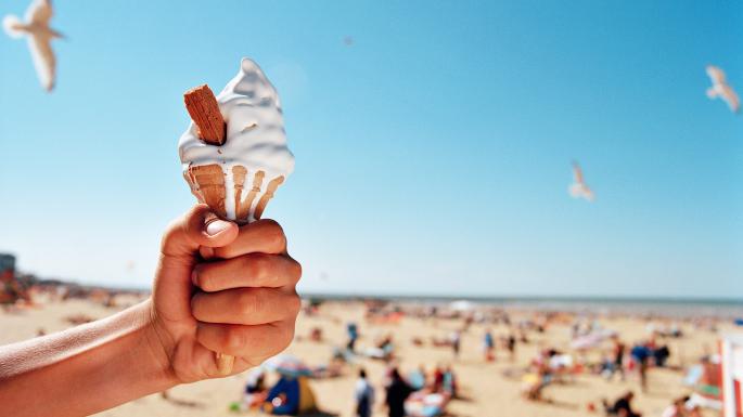 hand holding an ice cream with a beach in background