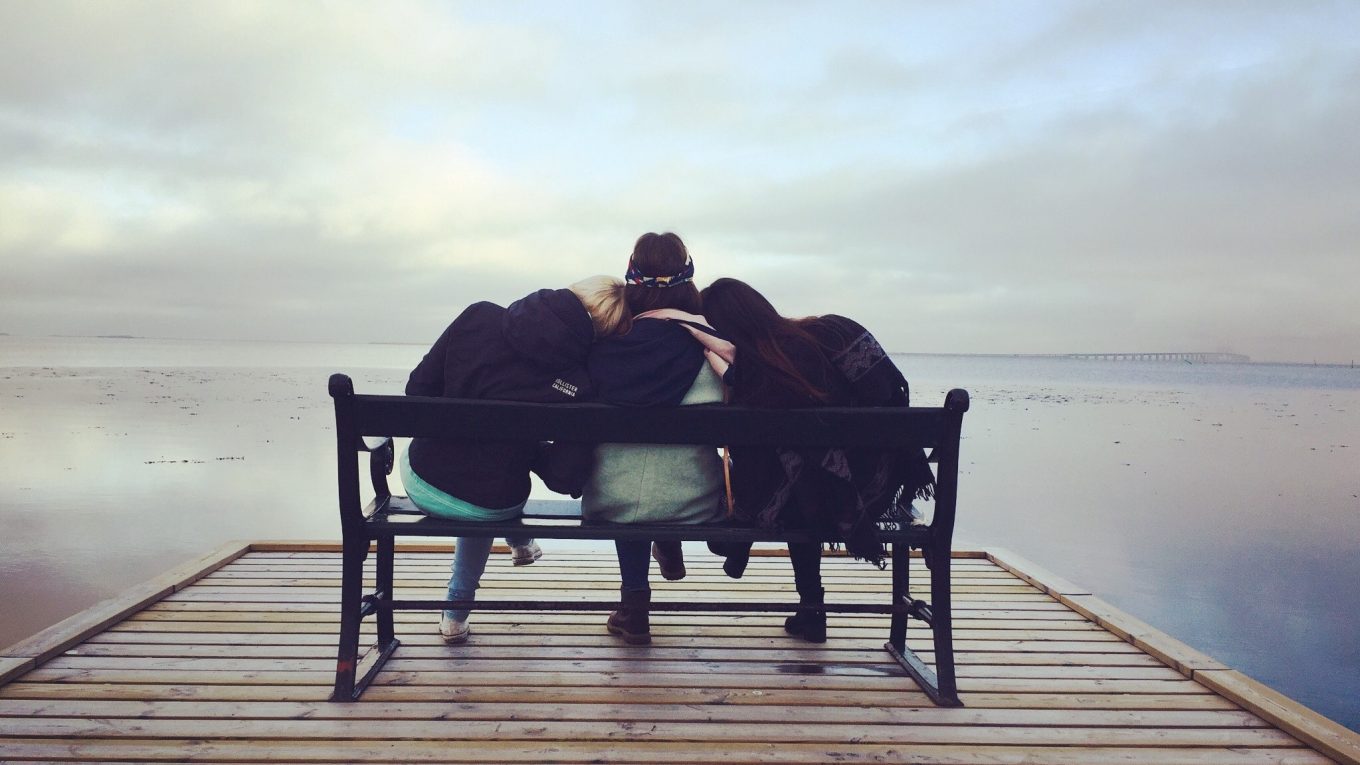 women sitting on a bench facing the sea