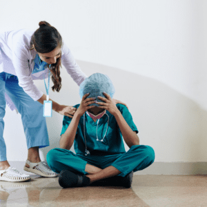 Nurse sat on floor with her head in her hands looking stressed, while a collegue comforts her 